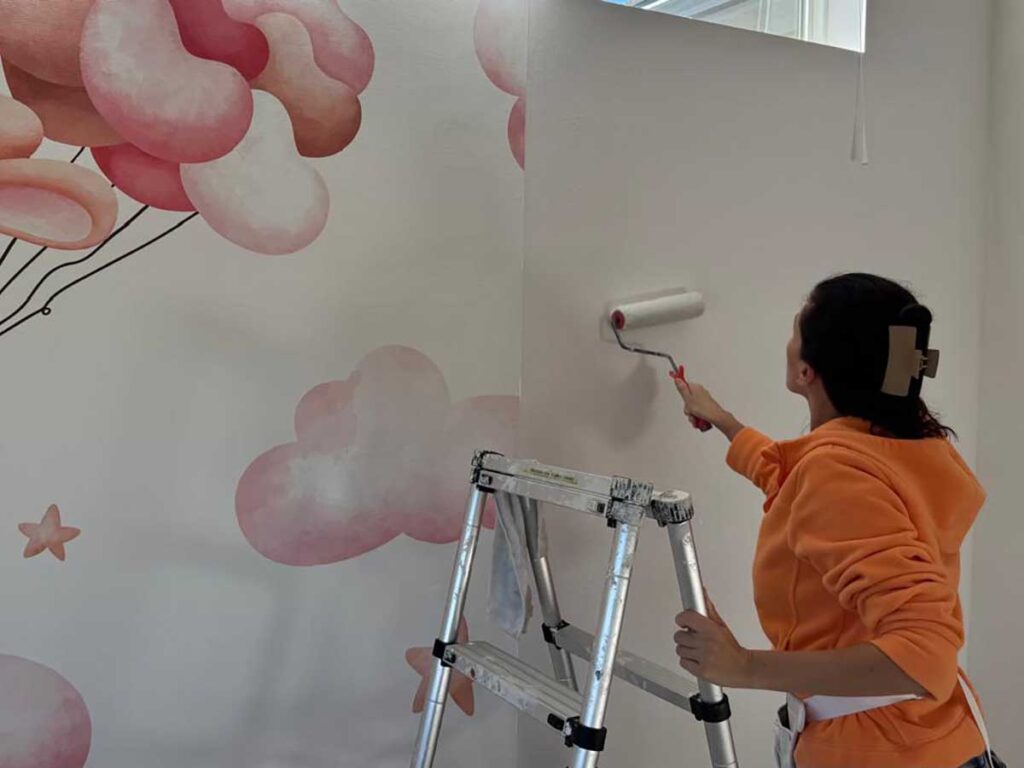 Wallpaper installation process in Denver metro area with installer applying primer before mural installation
