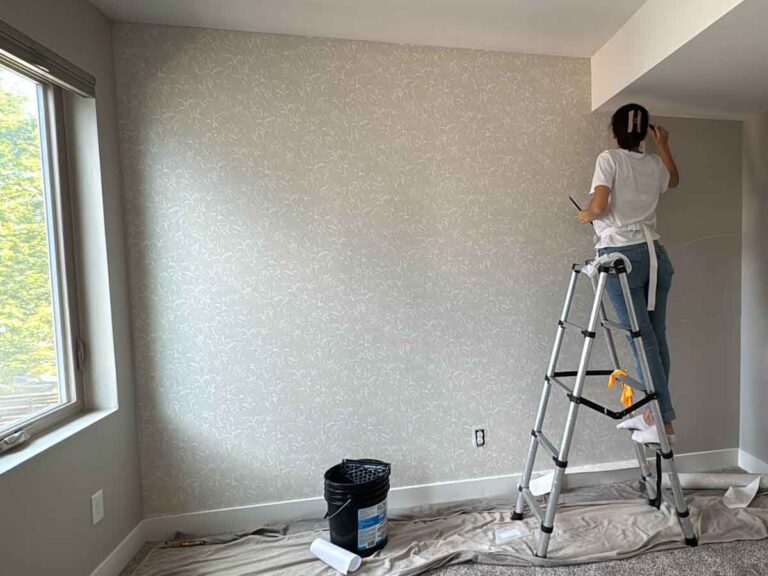 Professional wallpaper installer working on bedroom wall in Denver metro area using ladder for precise pattern alignment