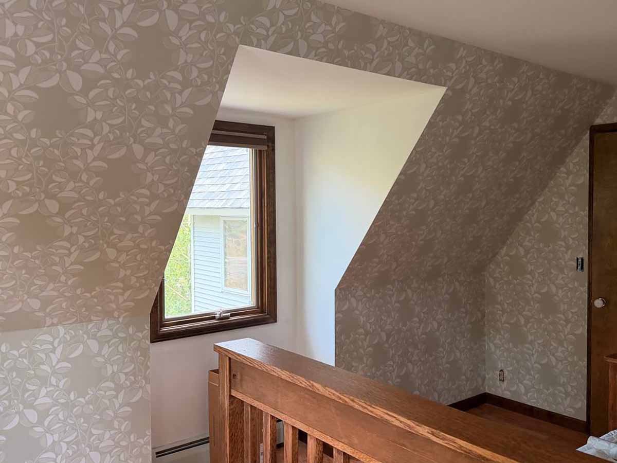 Professional wallpaper installation in Frederick, Colorado featuring a subtle botanical wallpaper in an upper-level hallway with sloped ceilings and angled walls.