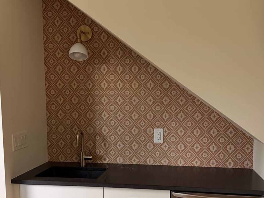 Professional wallpaper installation in a wet bar area beneath a staircase in Granby, Colorado featuring a geometric patterned wallcovering with precision cuts along the sloped ceiling.
