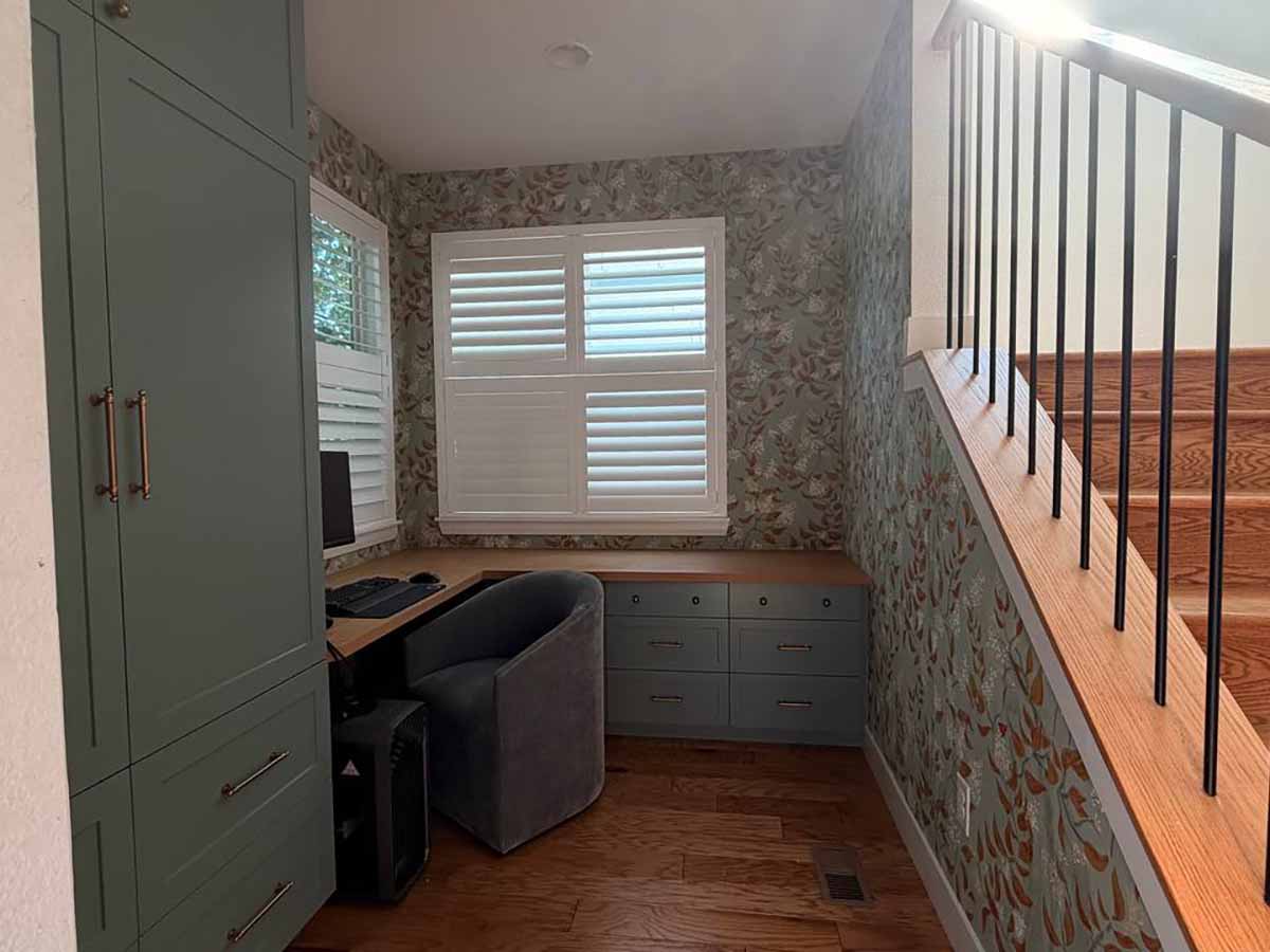 Home office wallpaper installation in Leadville, Colorado featuring a soft botanical pattern around custom built-in cabinetry, desk, windows, and staircase.