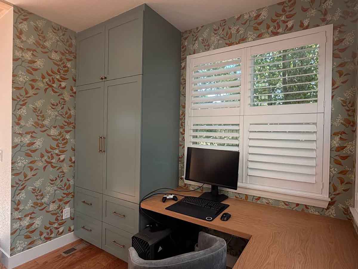 Home office wallpaper installation in Longmont, Colorado featuring an elegant botanical pattern around custom built-in cabinetry, desk, and plantation shutters.