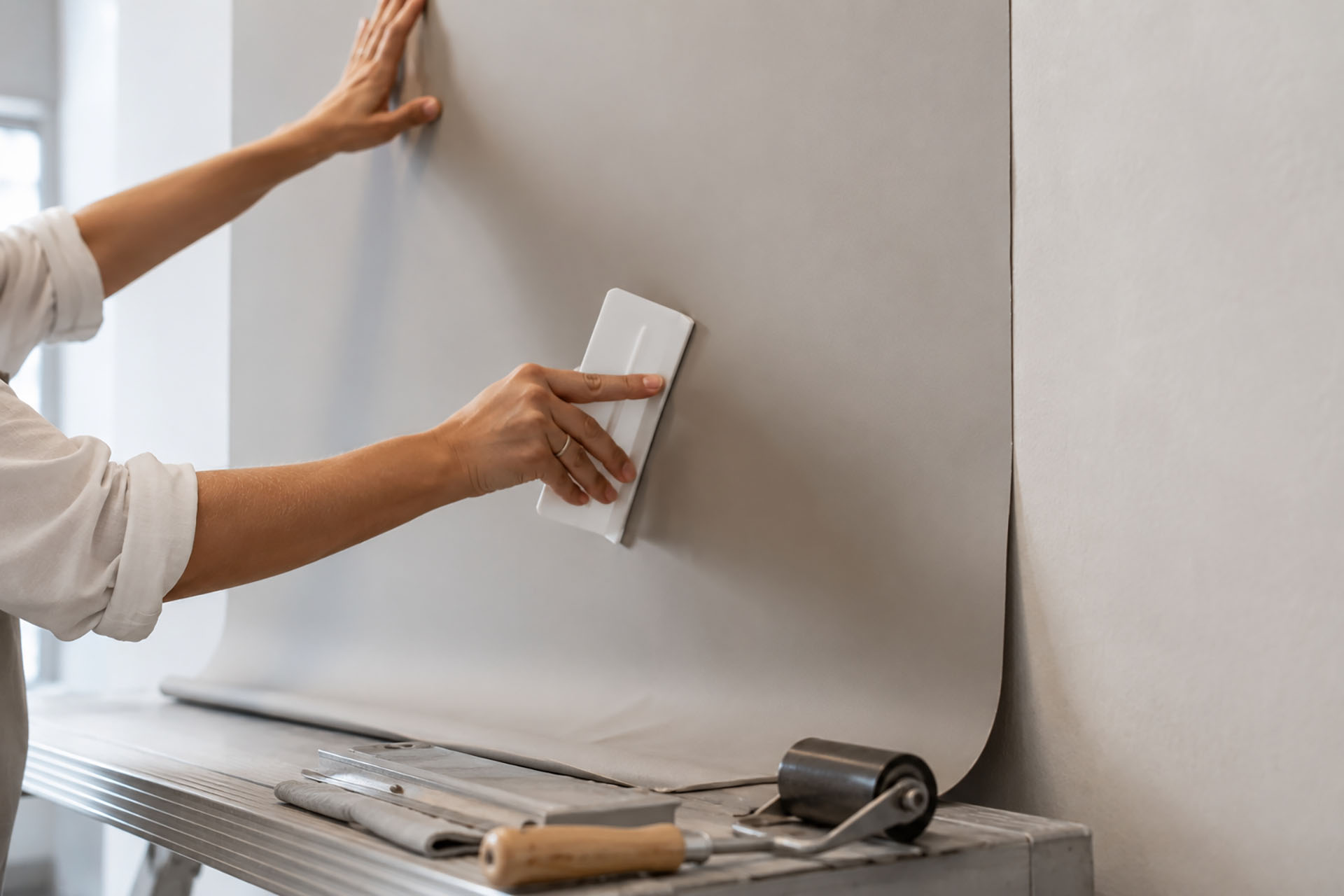 Professional installer smoothing smooth matte commercial vinyl wallcovering onto a wall using a plastic smoothing tool during a commercial wallcovering installation.