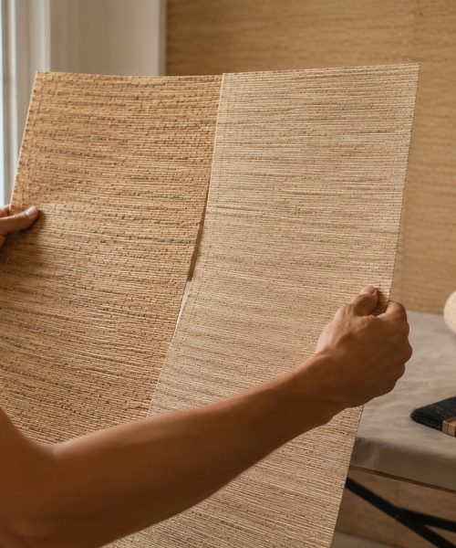 Installer comparing two sheets of natural grasscloth wallpaper to check color and texture variation before installation.