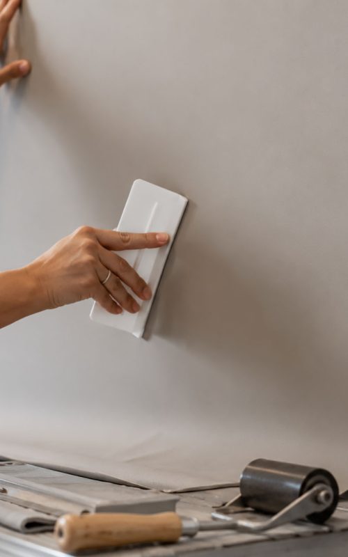 Professional installer smoothing smooth matte commercial vinyl wallcovering onto a wall using a plastic smoothing tool during a commercial wallcovering installation.